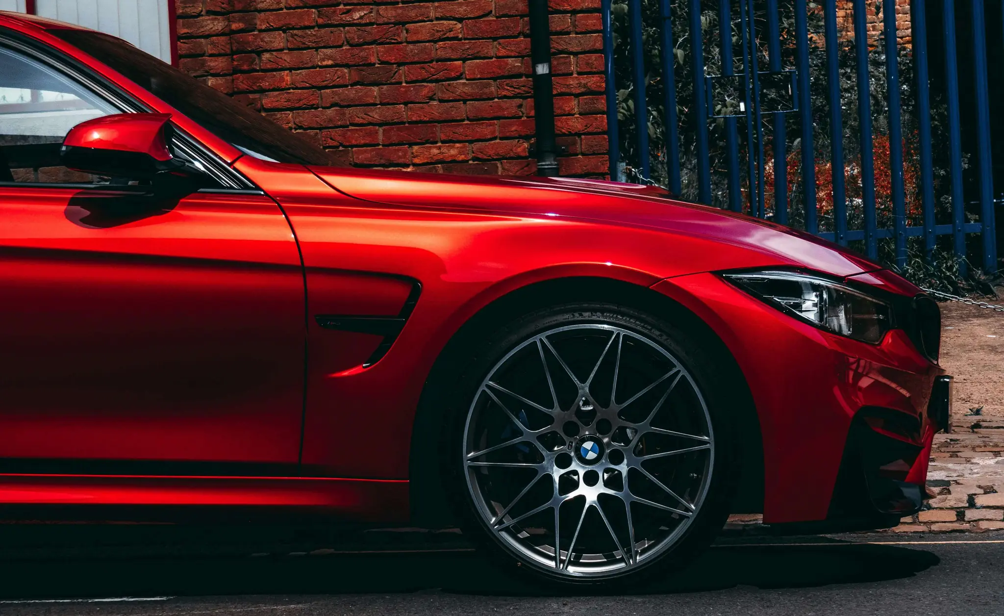 רכב BMW אדום מבריק עם חישוקי ספורט, מצולם מהצד עם רקע של קיר לבנים