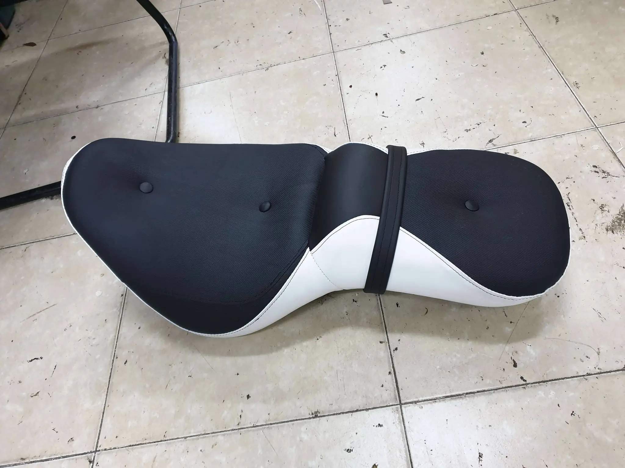 מושב אופנוע מרופד בצבע שחור ולבן על רצפת הסדנה