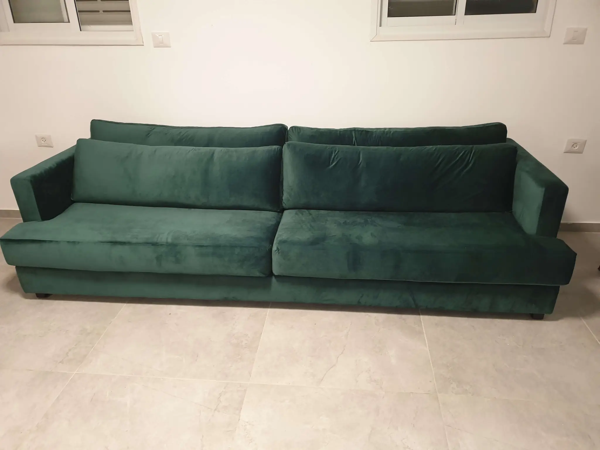 ספה ארוכה ומרופדת קטיפה בצבע ירוק כהה, עם כריות גב ורוחב מלא